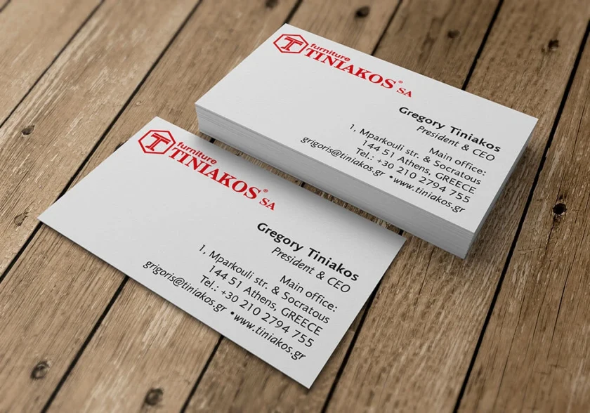 Επαγγελματικές κάρτες της Tiniakos Furniture σε λευκό και κόκκινο πάνω σε ξύλο