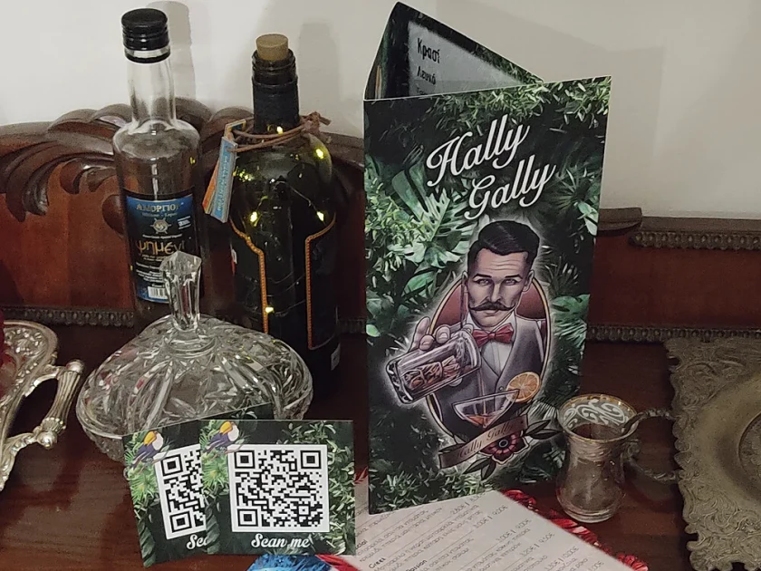 Ο τρίπτυχος κατάλογος του Hally Gally όρθιος δίπλα σε μπουκάλια και κάρτες QR