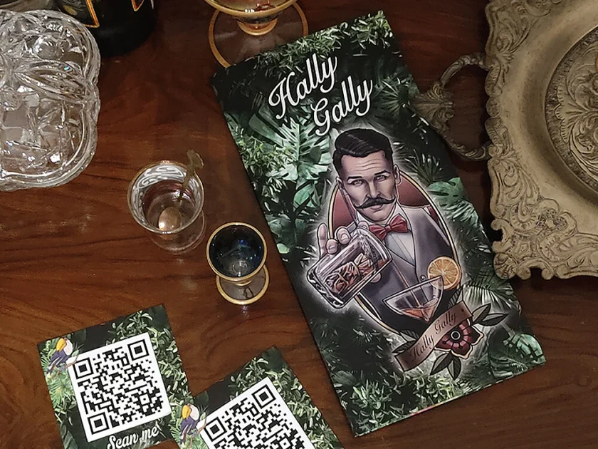 The Hally Gally menu with an illustration of a moustached bartender, next to QR cards on a wooden table
