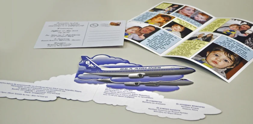 Christening invitation die-cut as an aeroplane, next to a card with photos of a child