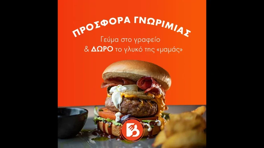 Frame from a promo video with a burger and fries and a Greek introductory offer: lunch at the office, with mum’s dessert as a gift